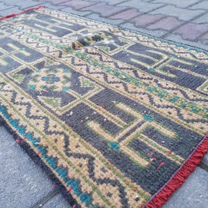 Könnte beinhalten: Ein kleiner, rechteckiger Teppich mit einem geometrischen Muster in Blautönen, Grün, Beige und Rot. Der Teppich hat einen Fransenrand.