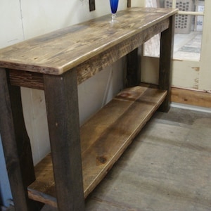 May include: A rustic wooden console table with a dark stained base and a natural wood top. The table has a lower shelf for storage.