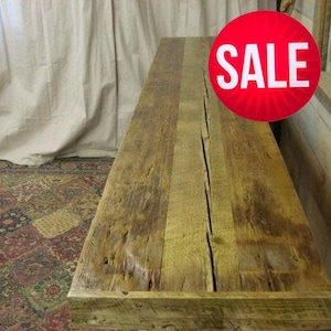 May include: A rustic, rectangular wooden table made from reclaimed wood. The table has a natural, weathered appearance with visible wood grain and a prominent crack running down the center. A red circle with the word "SALE" is visible.