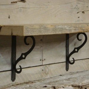 May include: A rustic wooden shelf with two black metal scroll brackets. The shelf is made of reclaimed wood and has a natural, weathered finish.