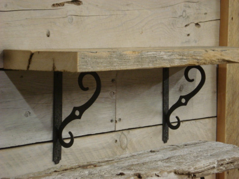 May include: A rustic wooden shelf with two black metal scroll brackets. The shelf is made of reclaimed wood and has a natural, weathered finish.
