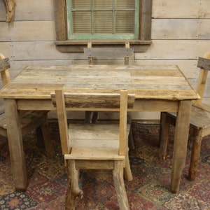 May include: A rustic wooden dining table set with four chairs. The table and chairs are made from reclaimed wood with a natural finish. The table has a rectangular top and four legs. The chairs have a simple design with a back and four legs.