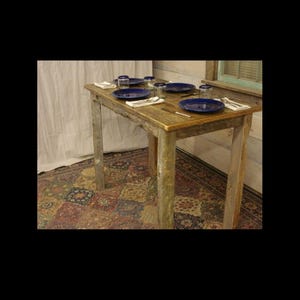 May include: A rustic wooden dining table set for four with blue plates, clear glasses, and silverware. The table has a natural wood finish and sits on a patterned rug. The table is approximately 48 inches long.