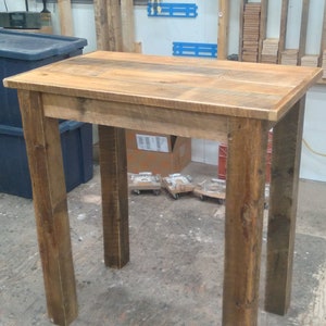May include: A rustic wooden table with a natural wood finish. The table has a rectangular top and four legs. The table is made of reclaimed wood and has a unique, handcrafted look.