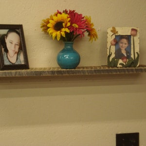 Peut inclure: Une étagère en bois rustique avec deux photos encadrées et un vase de fleurs. Les photos sont dans des cadres noirs et le vase est de couleur bleu vif. L'étagère est en bois de récupération et a une finition naturelle.