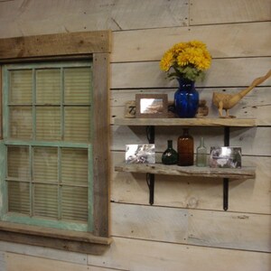 May include: Rustic wooden shelves with a blue glass vase filled with yellow flowers, a wooden bird figurine, and various bottles. The shelves are mounted on a whitewashed wood wall with a window to the left.