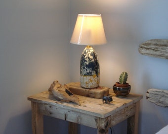 May include: A rustic wooden side table with a lamp, a small potted cactus, and a small metal figurine. The lamp has a white lampshade and a unique base made from a repurposed buoy.
