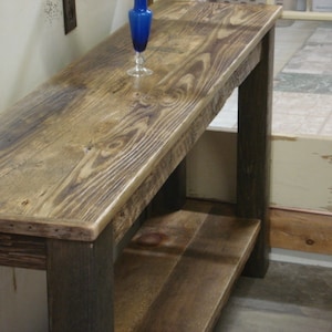 May include: A rustic wooden console table with a dark stained finish and a lower shelf. The table has a distressed look and is made of reclaimed wood.