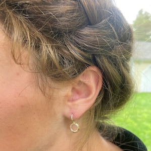 May include: A pair of gold hoop earrings with a hammered texture. The earrings are small and delicate, and they are hanging from the earlobe.