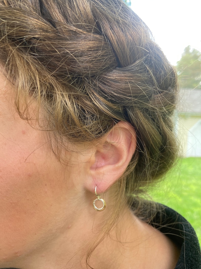 May include: A pair of gold hoop earrings with a hammered texture. The earrings are small and delicate, and they are hanging from the earlobe.