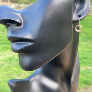May include: A silver hoop earring on a black mannequin head. The earring is a simple circle shape.