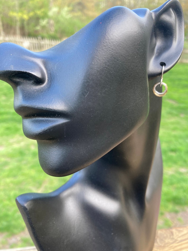 May include: A silver hoop earring on a black mannequin head. The earring is a simple circle shape.