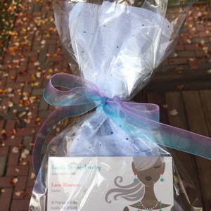 May include: A white gift bag with a blue and pink ribbon, containing a business card for Lara's Theme Jewelry. The business card features a woman with long hair wearing a turquoise necklace and earrings. The text on the card reads "Lara's Theme Jewelry", "larastheme.com", "Lara Stawasz", "Owner", "16 Proctor Hill Rd", "Hollis, NH 03049", "603-465-5389", and "ras@aol.com".