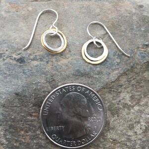 May include: A pair of silver earrings with a gold circle inside each earring. The earrings are small and delicate, and they are perfect for everyday wear.