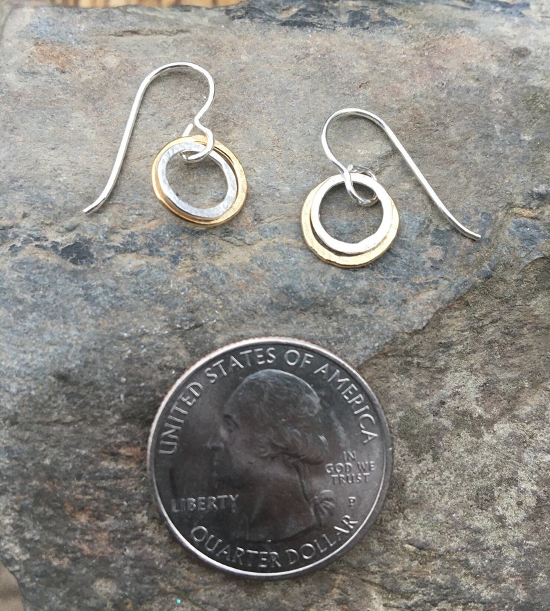 May include: A pair of silver earrings with a gold circle inside each earring. The earrings are small and delicate, and they are perfect for everyday wear.