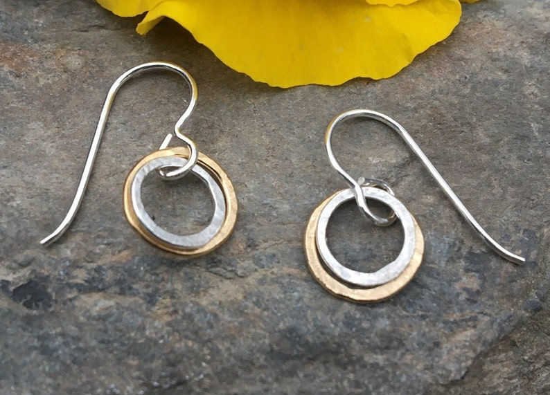 May include: A pair of silver dangle earrings with a hammered gold circle inside a larger silver circle.