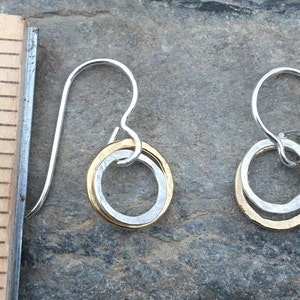 May include: A pair of silver dangle earrings with a gold circle inside a larger silver circle.
