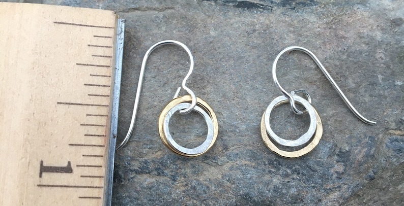 May include: A pair of silver dangle earrings with a gold circle inside a larger silver circle.