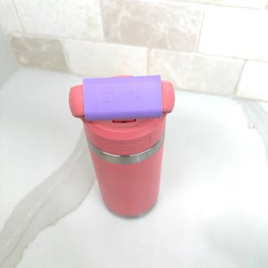 May include: A pink Yeti tumbler with a purple silicone lid that says "Emma" on it.