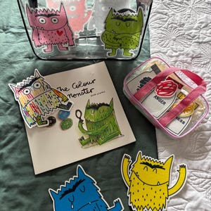 May include: A clear tote bag with black trim and monster illustrations. The bag contains monster-themed items, including a book titled "The Colour Monster" and several monster cutouts in various colours. A smaller bag with emotion cards is also visible.