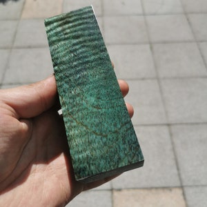 Könnte beinhalten: Nahaufnahme eines grünen Holzrohlings mit einem wirbelnden Maserungsmuster. Das Holz ist glatt und poliert.
