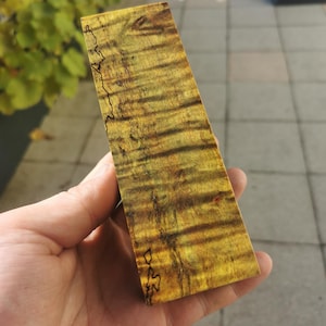 Könnte beinhalten: Nahaufnahme eines Stückes Holz mit einem gelben und braunen Farbmuster. Das Holz hat eine natürliche Maserung und ist glatt.