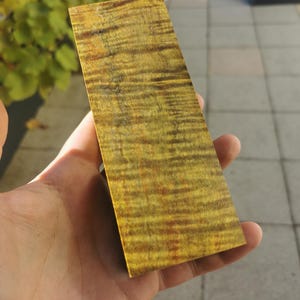 Könnte beinhalten: Nahaufnahme eines Stückes Holz mit einer gelben, braunen und schwarzen Maserung. Das Holz ist glatt und poliert.