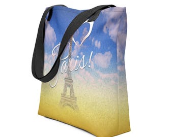 Könnte beinhalten: Tragetasche mit einem Landschaftsdesign mit dem Eiffelturm und dem Wort "Paris!" vor einem blauen Himmel mit Wolken. Die Tasche hat schwarze Träger und einen gelb-blauen Farbverlauf.