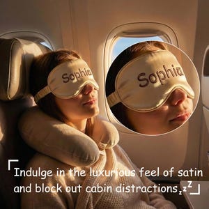 Puede incluir: Una máscara para dormir de satén beige con el nombre "Sophia" bordado en marrón. La máscara la lleva una persona en un avión, junto con una almohada para el cuello. La imagen también incluye el texto "Indulge in the luxurious feel of satin and block out cabin distractions."