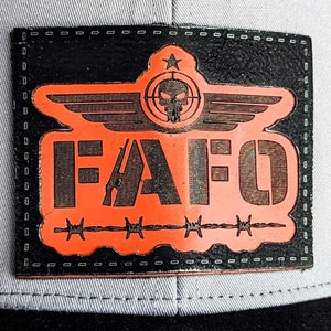 May include: A black and orange patch with the text "FAFO" in a stylized font. The patch features a skull with wings and a barbed wire design.