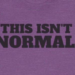 Może przedstawiać: Fioletowa koszulka z napisem „THIS ISN'T NORMAL.” w pogrubionej, czarnej czcionce. Koszulka ma melanżową fakturę.