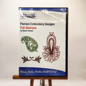 Könnte beinhalten: Eine DVD-Hülle mit "Floriani Embroidery Designs: Fall Abstracts" von Walter Floriani. Das Cover zeigt grüne, braune und kastanienbraune Stickmuster, darunter Paisley- und Blumenmuster. Das Floriani-Logo befindet sich oben.