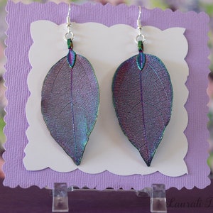 May include: A pair of iridescent leaf earrings with silver hooks. The leaves are translucent and have a purple, blue, and green shimmer.