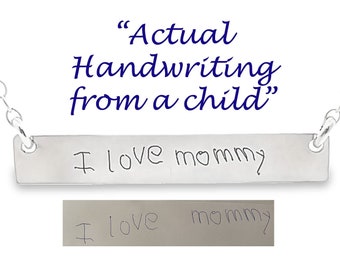 May include: Silver necklace with a bar pendant engraved with the words "I love mommy" in a child's handwriting. The handwriting is shown below the pendant.