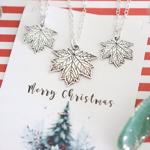 May include: Three silver maple leaf necklaces on a white card with the text "Merry Christmas".