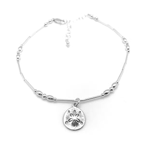 May include: Silver anklet with a sand dollar charm. The anklet has a delicate chain with small beads and a lobster clasp.