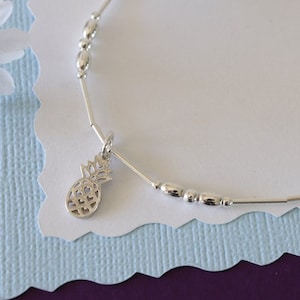 May include: A silver anklet with a pineapple charm and small silver beads. The anklet is on a white background.