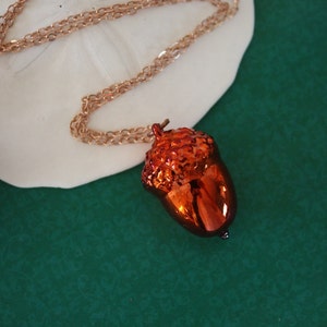 May include: A gold chain necklace with a shiny orange acorn pendant.
