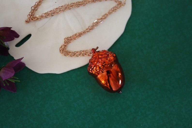 May include: A gold chain necklace with a shiny orange acorn pendant.