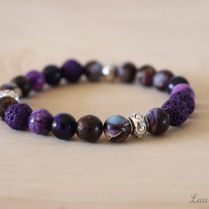 May include: Purple, brown, and black beaded bracelet with a silver spacer bead. The bracelet is made with lava rock, amethyst, and tiger's eye beads.