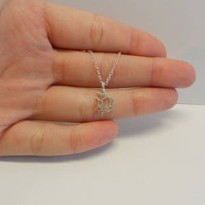 Op de afbeelding: Een zilveren ketting met een delicate, ingewikkelde hanger in de vorm van een vis. De hanger is gemaakt van fijn zilverdraad en heeft een delicaat, luchtig ontwerp.