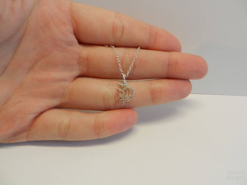 Op de afbeelding: Een zilveren ketting met een delicate, ingewikkelde hanger in de vorm van een vis. De hanger is gemaakt van fijn zilverdraad en heeft een delicaat, luchtig ontwerp.