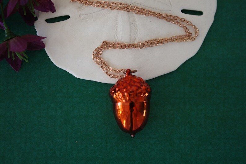 May include: A gold chain necklace with an orange acorn pendant. The pendant is shiny and has a detailed design.