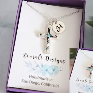 May include: Two silver necklaces with cross pendants in a purple box. The cross pendants are made of turquoise and other stones. The necklaces are from Laura Li Designs and are handmade in San Diego, California.