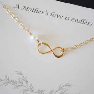 May include: A gold infinity symbol necklace with a single white pearl charm. The necklace is on a white card with the text "A Mother's love is endless".