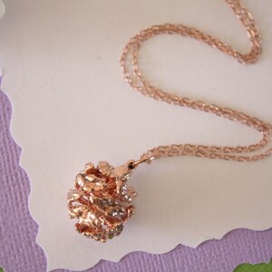 May include: A rose gold necklace with a delicate chain and a textured, rose gold pendant in the shape of a ball.