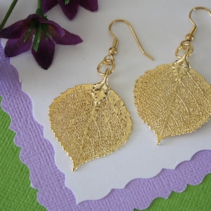 Peut inclure: Boucles d'oreilles en feuille d'or avec un design délicat et détaillé d'une feuille. Les boucles d'oreilles sont suspendues à des crochets dorés.