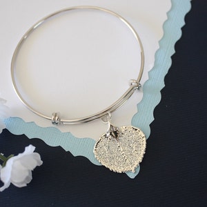 May include: A silver expandable bangle bracelet with a silver heart-shaped leaf charm. The charm has a detailed leaf design.