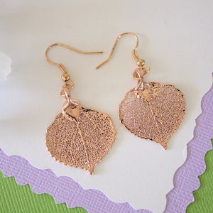 May include: A pair of gold-toned earrings featuring delicate, leaf-shaped pendants. The leaves have a detailed, intricate design and appear to be made from real leaves that have been preserved and coated in gold.
