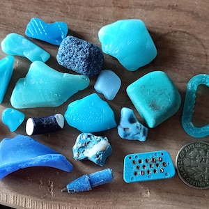 Könnte beinhalten: Eine Sammlung von blauem und grünem Meerglas, einige mit rauer Textur, und ein paar andere kleine blaue Objekte, darunter ein kleines blaues Plastikobjekt mit einem Gittermuster, ein blaues Plastikobjekt in Form eines Hufeisens und ein kleines blaues Plastikobjekt in Form eines Bleistifts.